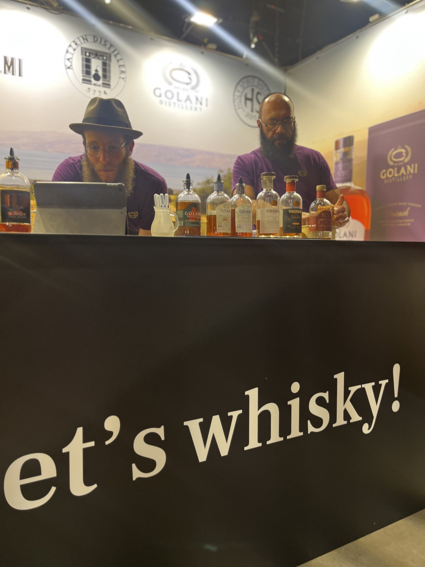 Two exhibitors at a drinks stand with a Let's Whisky sign.