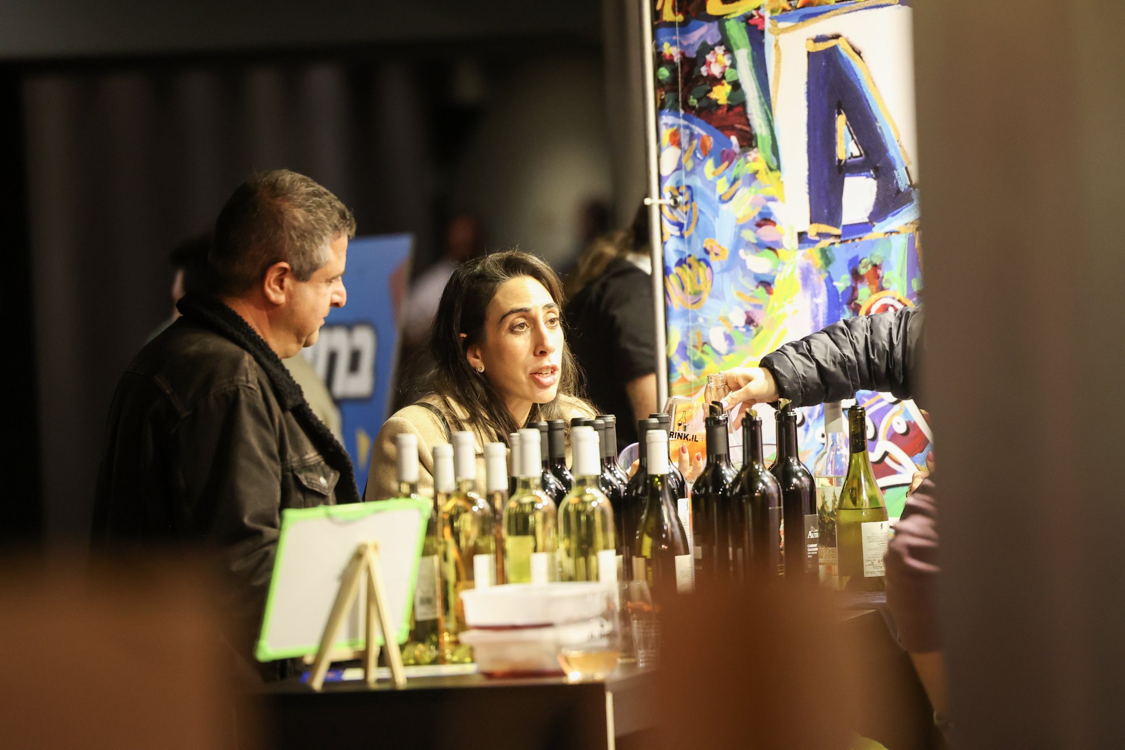 Exhibitors talk with visitors across a bottle-lined counter.