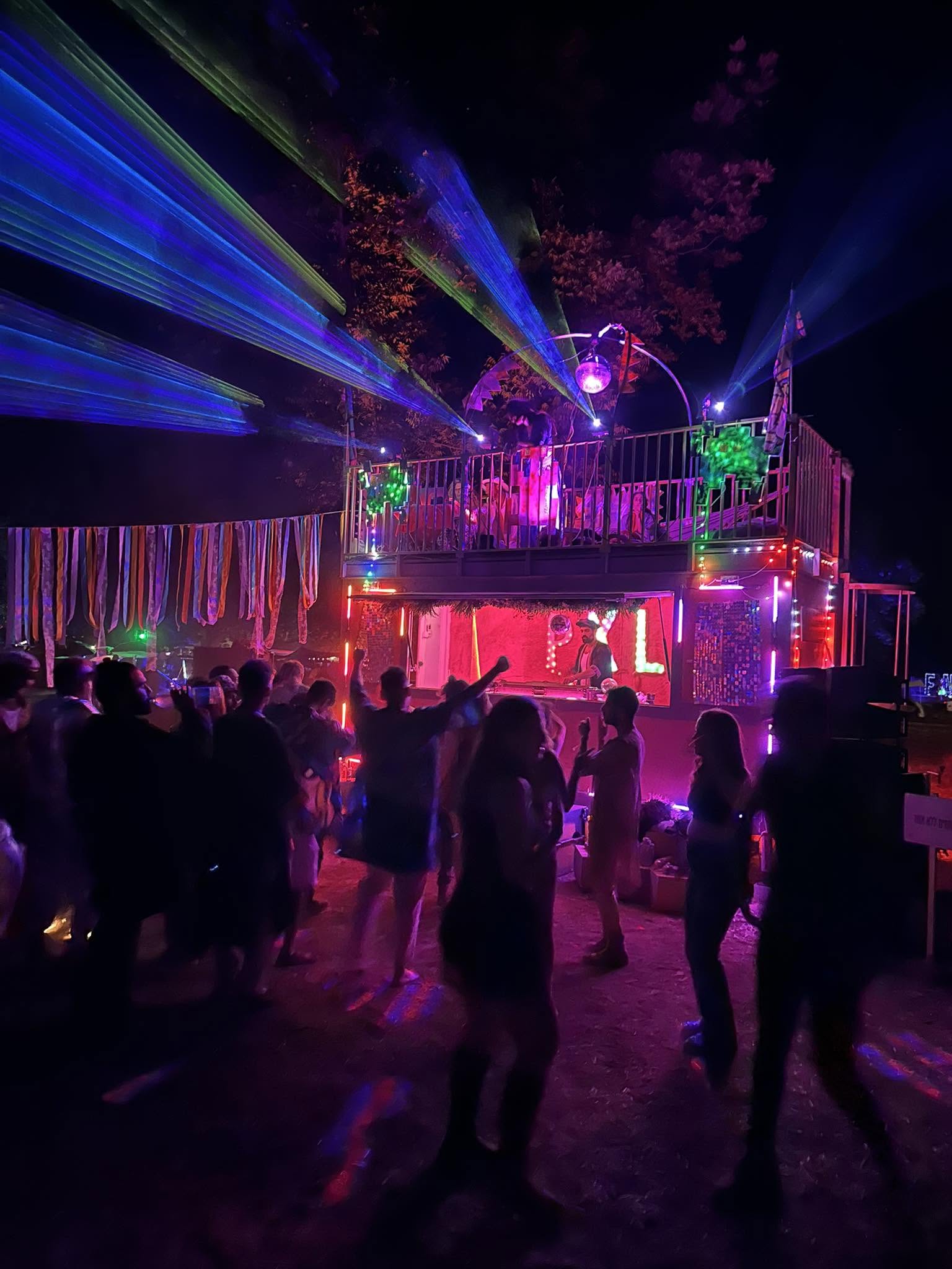 A crowd gathers before a stage with colourful laser beams.