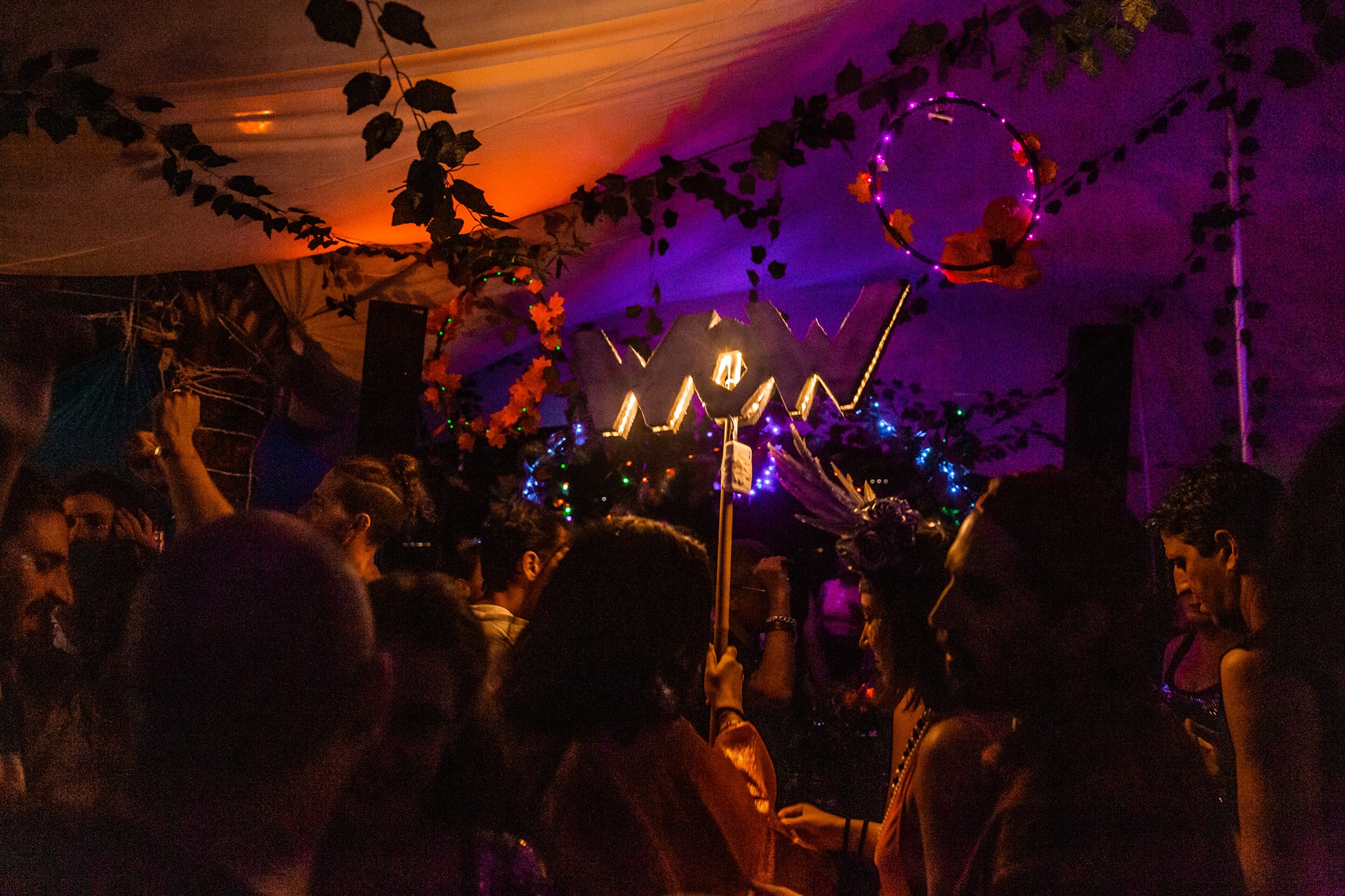 A crowd dances beneath purple and orange lighting inside a tent.