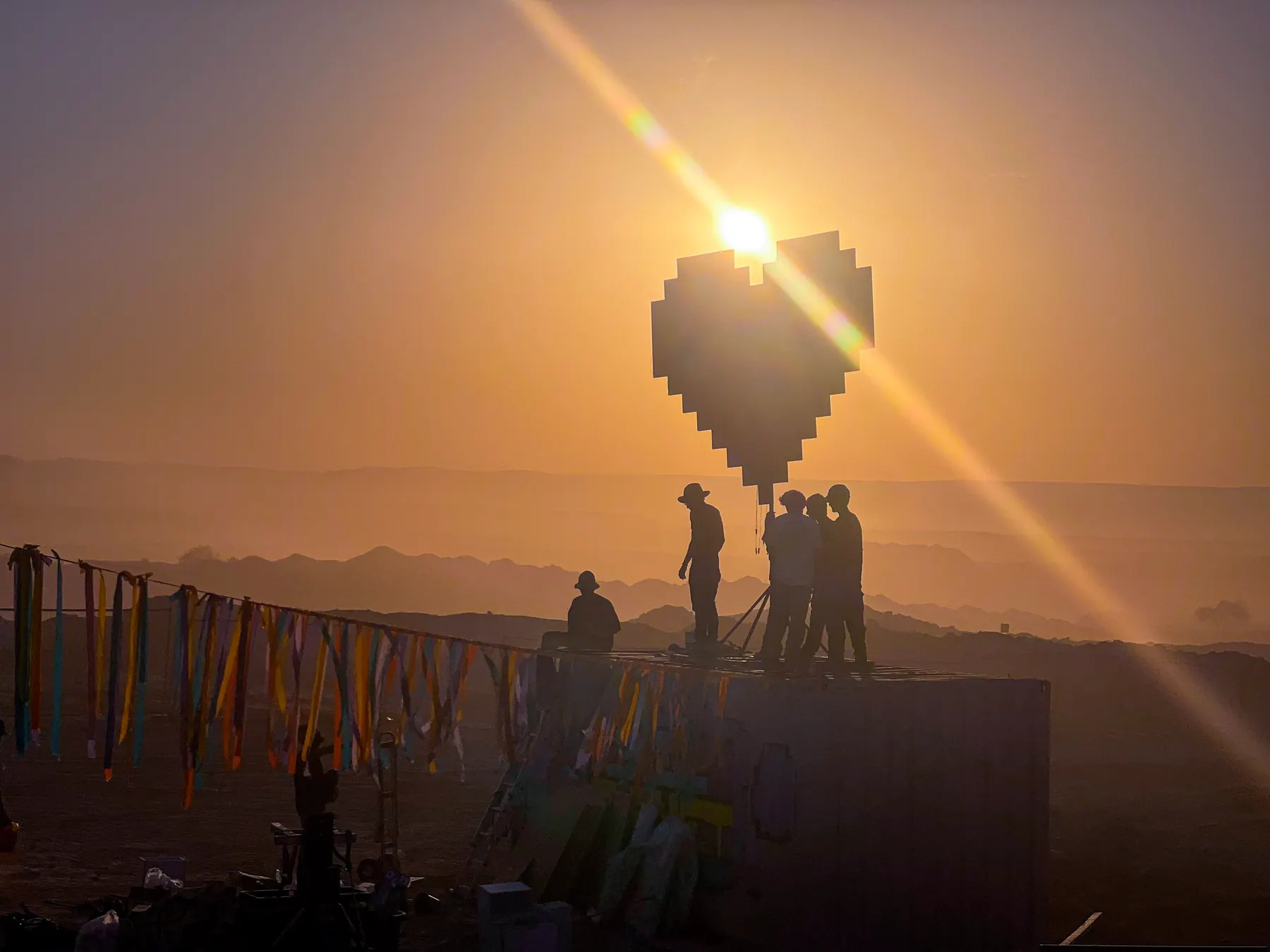 People stand on a structure beneath a heart-shaped installation at sunset.