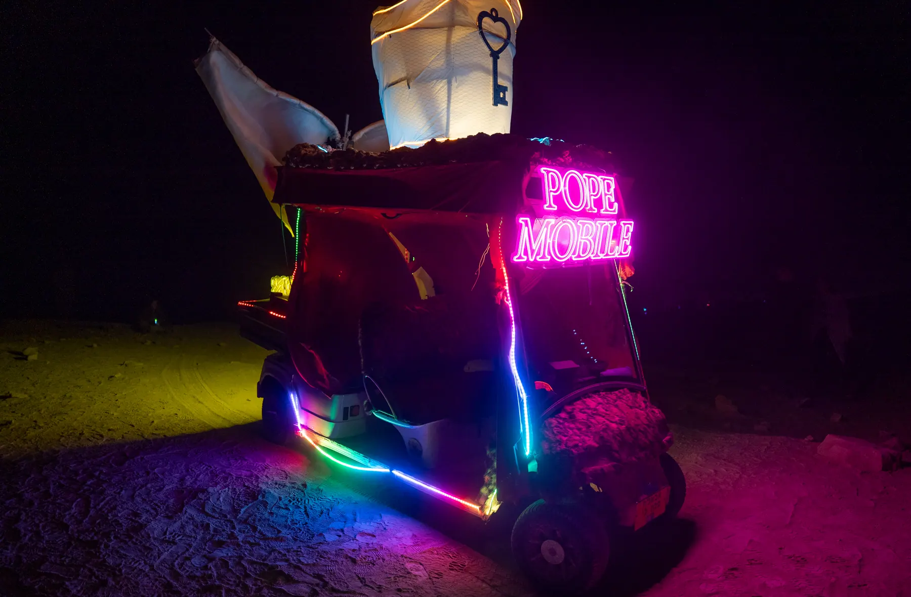 A small art vehicle decorated with colourful neon lights at night.