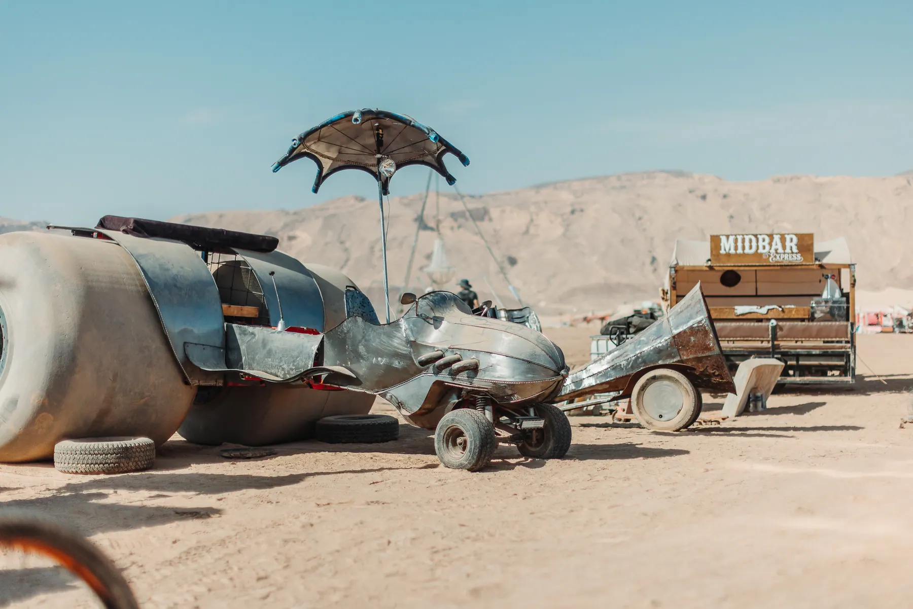 A metal art vehicle with large wheels in the daytime desert.