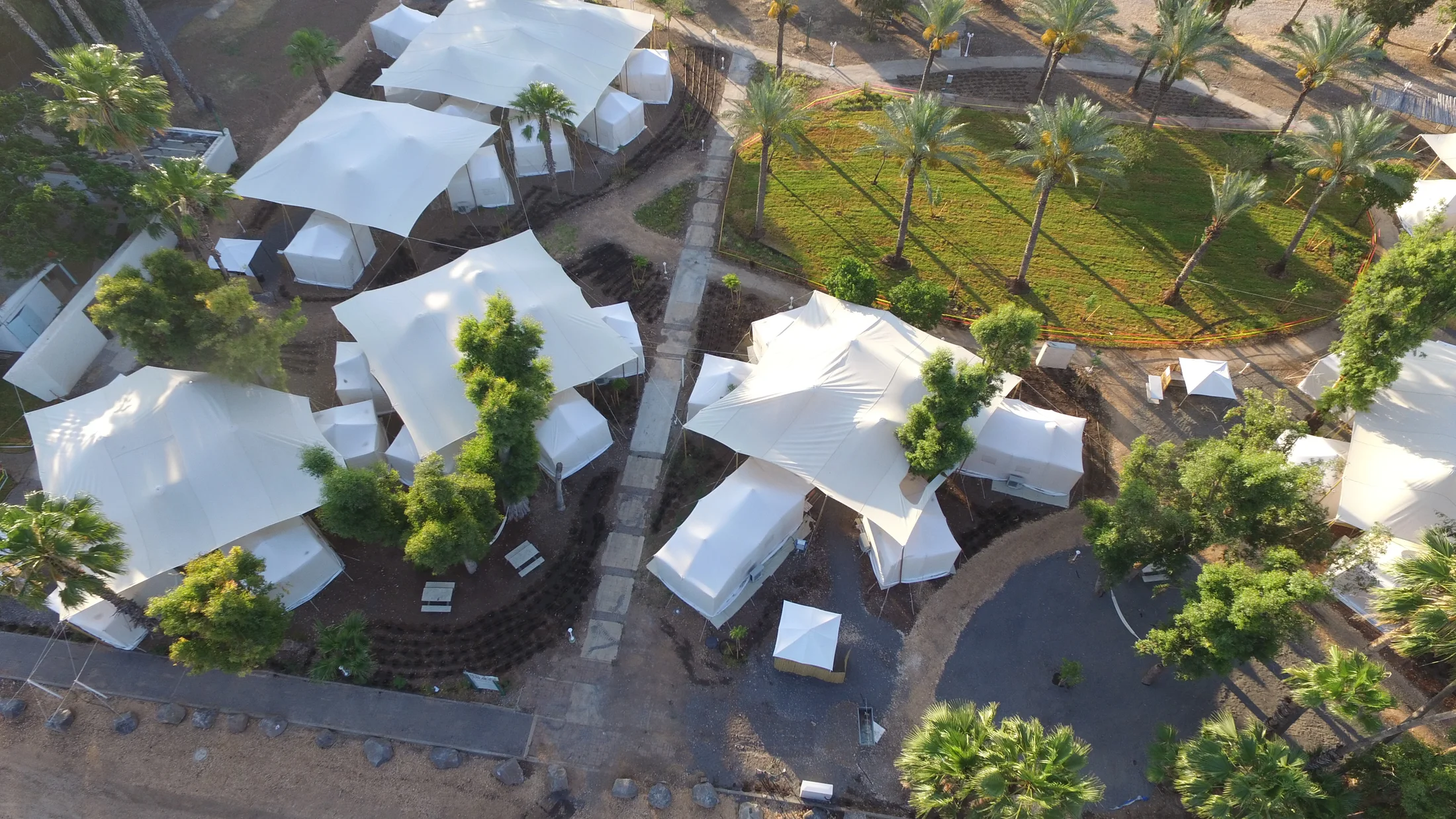 Aerial view of white tent cabins among trees near the beach.